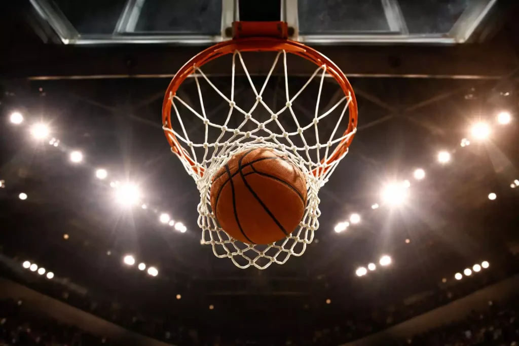 Basketbal vliegt door de ring en het net in een verlichte arena, gefotografeerd van onderaf