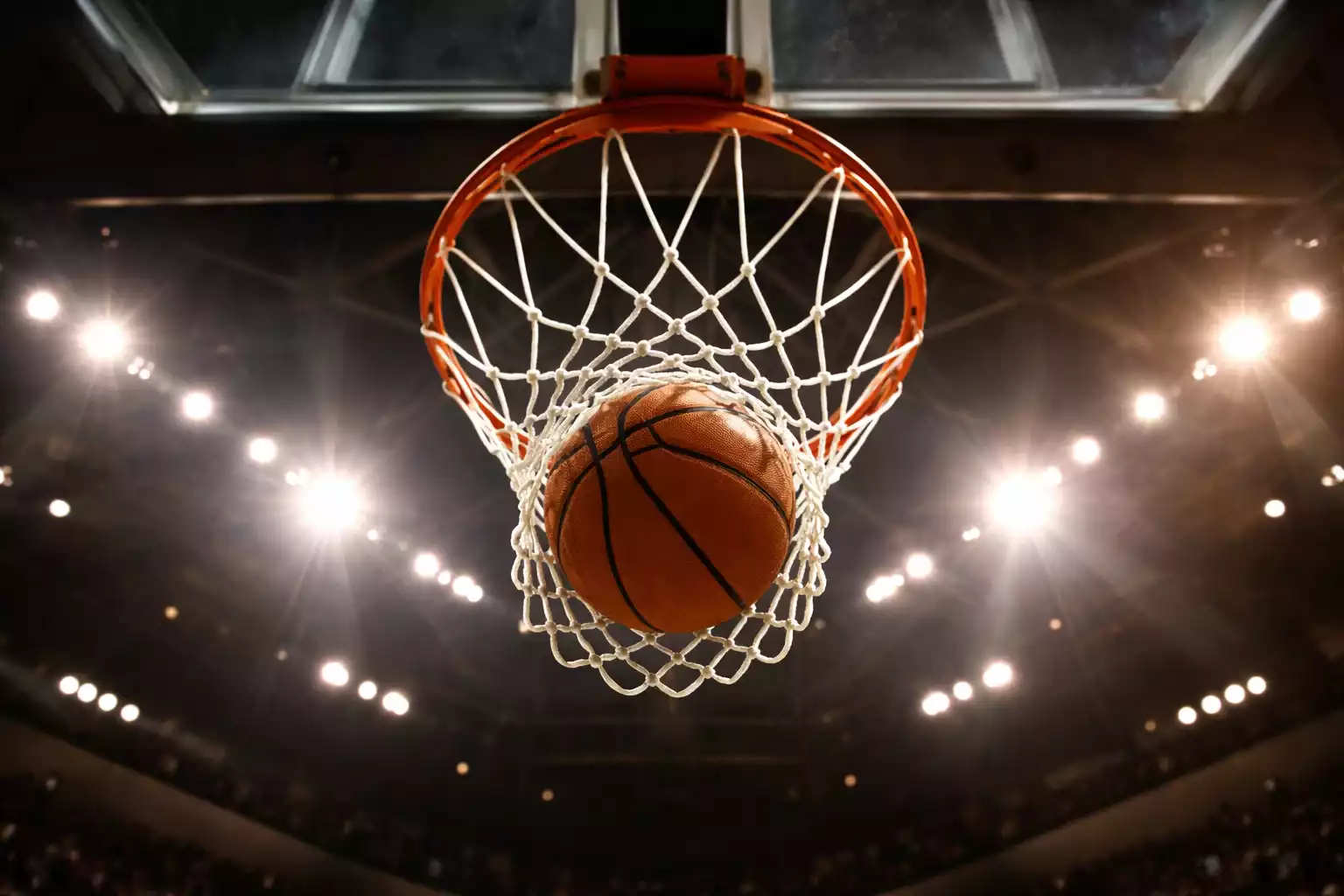 Basketbal vliegt door de ring en het net in een verlichte arena, gefotografeerd van onderaf