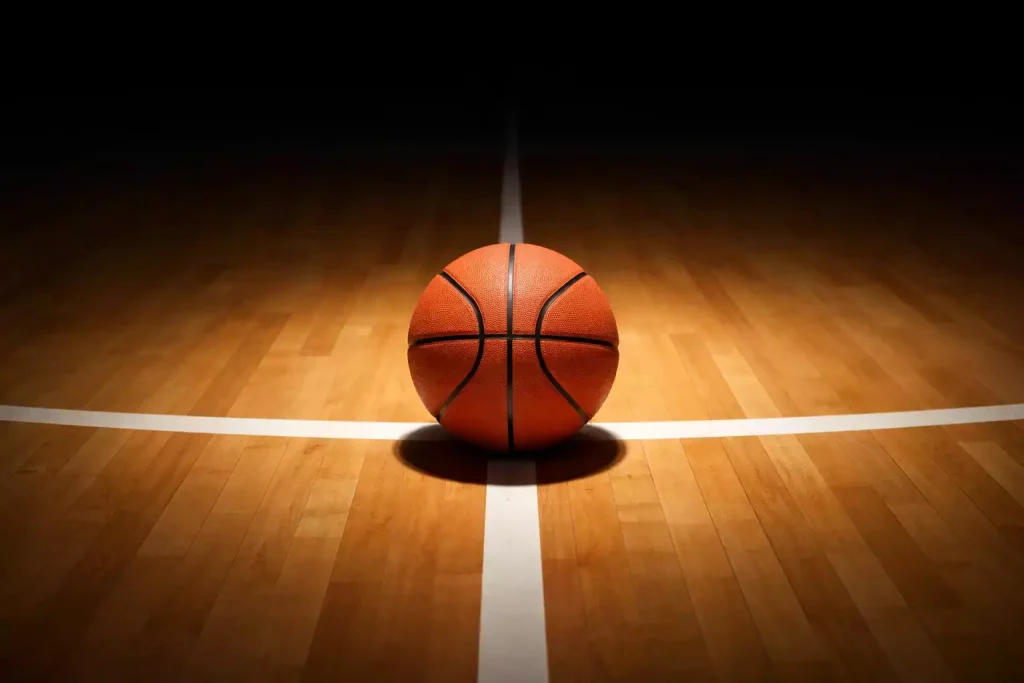 Close-up van een basketbal op een verlicht hardhouten veld met scherpe lijnen en schaduwen